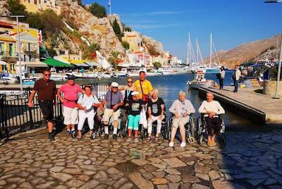 A group of people on the beach. Three are standing, one has a prosthetic leg and the other two are on beach wheelchairs. 