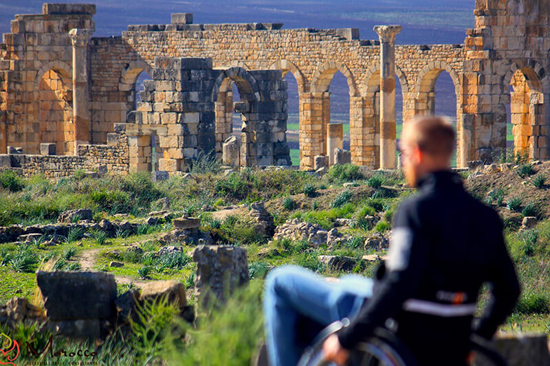 Panoramic photo of ancient ruins in Morocco with a man in a wheelchair out of focus.