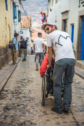 A wheelchair user is being assisted in navigating uneven Cusco terrains