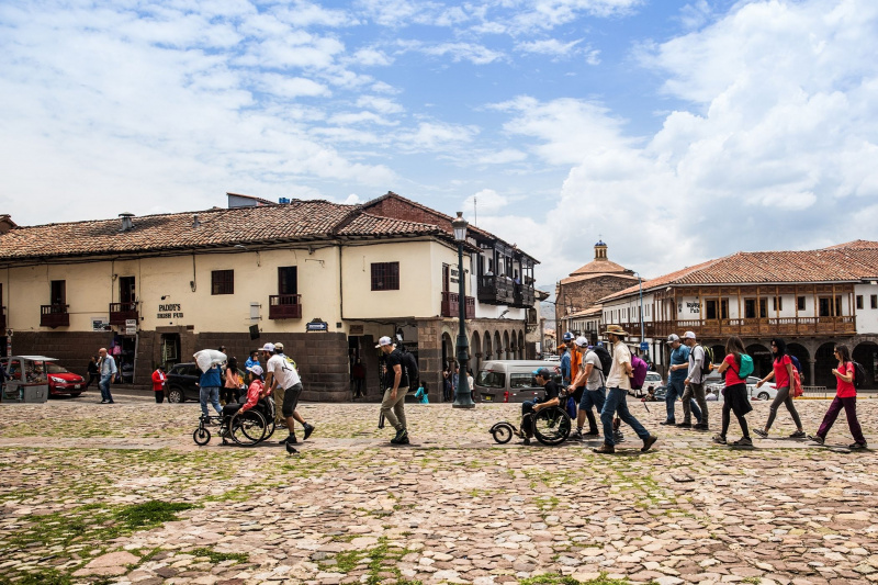 Two wheelchair users are helped to navigate Cusco's uneven terrain
