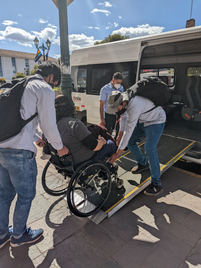 Assistants are helping a wheelchair user board the accessible van