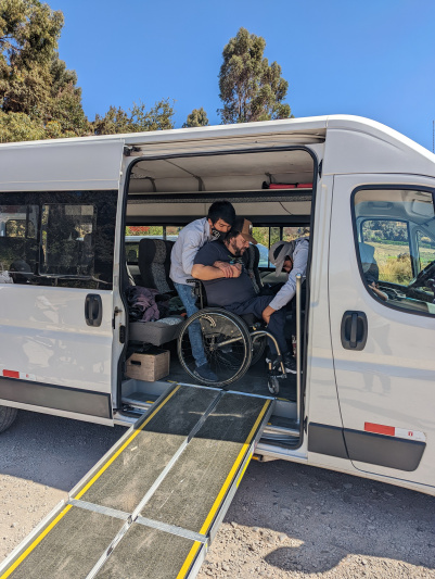 Assistants are helping a wheelchair user board the accessible van