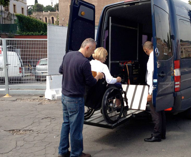 A staff member assists a person in a wheelchair to board an accessible vehicle