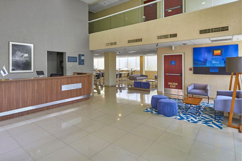 Hotel lobby with seating area, standing height front desk, and overhead balcony.