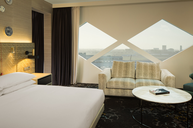 The accessible room has carpet flooring, a two-seater sofa, a coffee table, queen bed, and bedside light controls