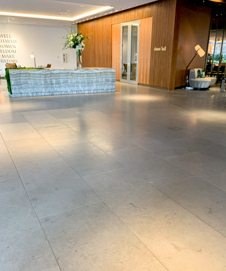 The wide, step-free lobby has very little furniture. There is long desk at one end of the room, with seating behind it.