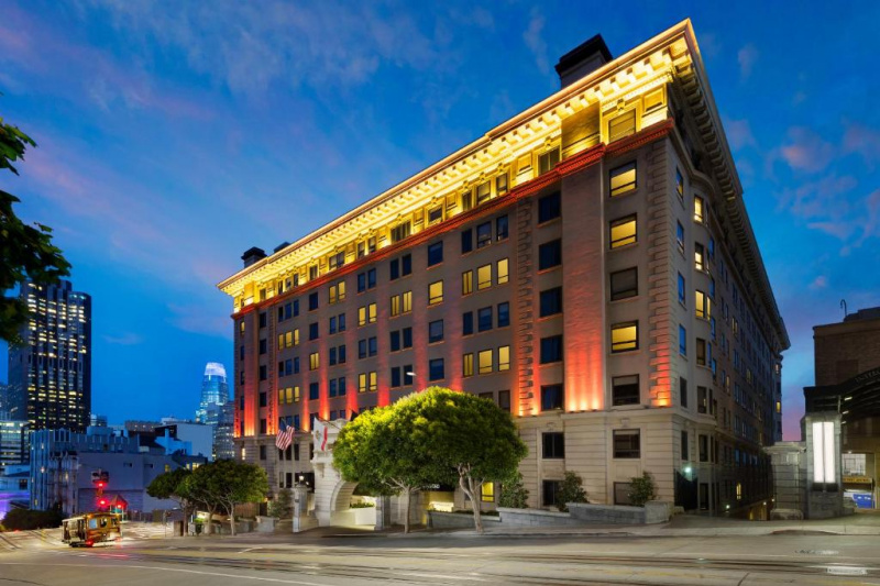 The exterior of the building shows a huge 7-story block built on a slight incline. There is a wide street in front of it and a large archway leads to the hotel entrance.