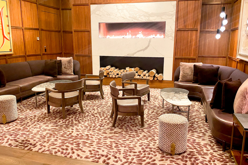 The wood-paneled seating area has a fireplace with sofas either side. There are coffee tables and chairs in front of the sofa.