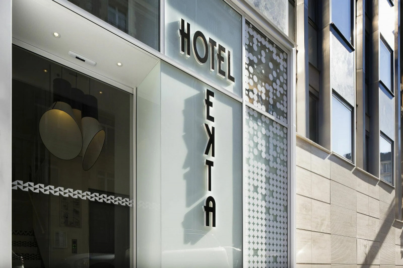 The entrance of the hotel has a white glass paneled facade. The hotel's name is large and in black.