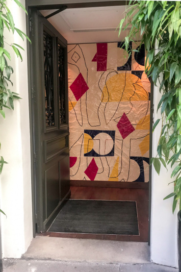 The open entrance door reveals a slight incline from the sidewalk and shows a large mural on the back wall.