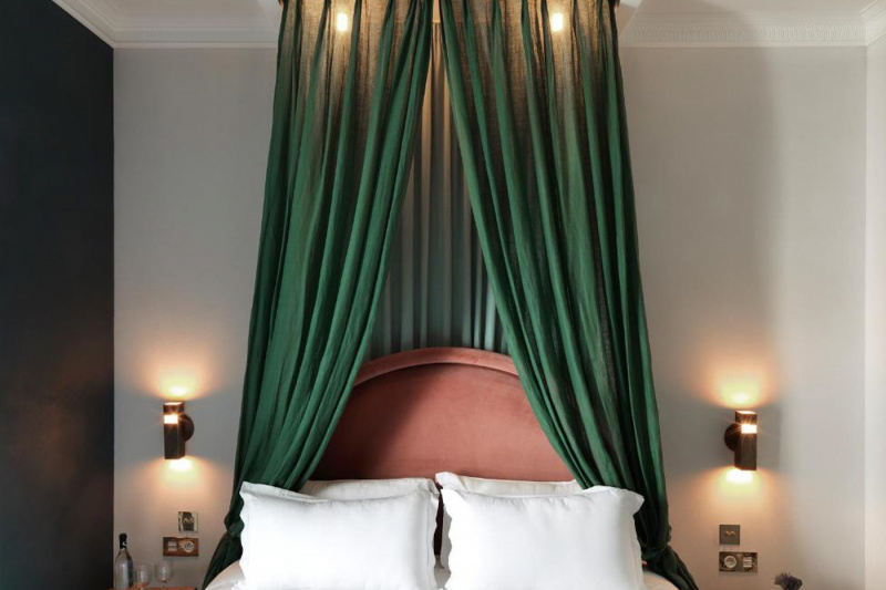 The Classic Room has a large, canopied bed. There are nightstands on either side of the bed. There are plug sockets and lights mounted on the wall.