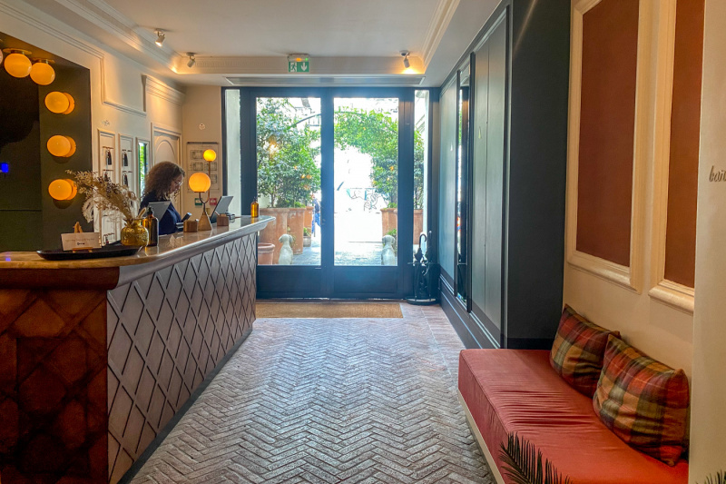 The lobby has a brick floor. The tall reception desk is to one side. On the other side, is a sofa. to the front, are the entrance doors.
