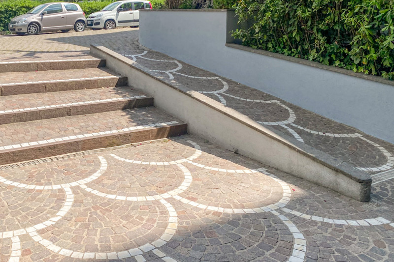 This outdoor cobble stoned area has steps with a ramp at the side. They lead to the road.