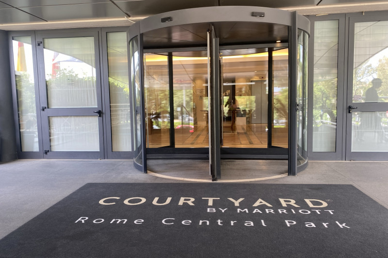 The step-free entrance to the Courtyard Marriott Central Park Rome, has a large revolving door. There are closed doors to either side.