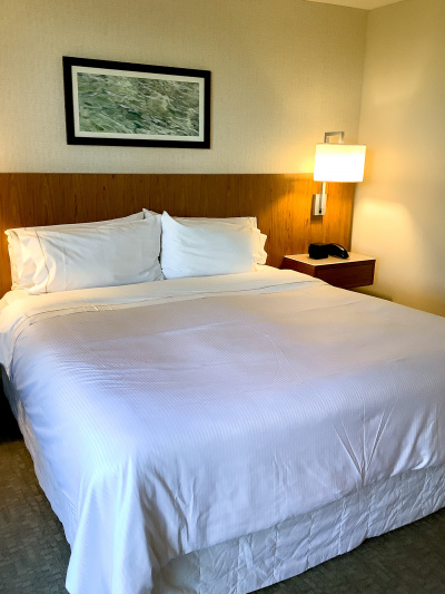King-sized bed with nightstands, white linen,a telephone,wall-mounted reading lamps and artwork on the wall.