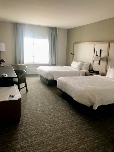 Suite showing 2 queen-sized beds with white linen, desk and chair, lamps and under window air-conditioner.