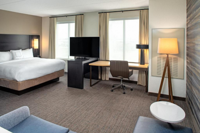 The 1 king studio has a king-sized bed with integral reading lamps, seating area with sofa, large windows, a flat screen TV, and a desk with office chair.