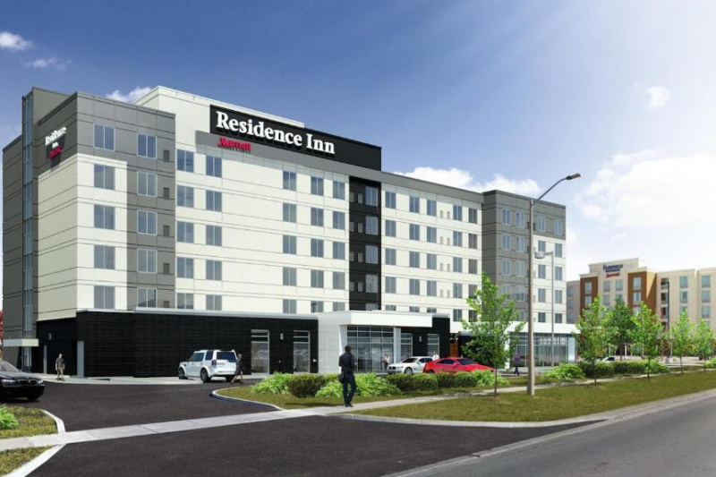 The Residence Inn is a modern 6-storey building with a drop-off point and parking area with trees and bushes.