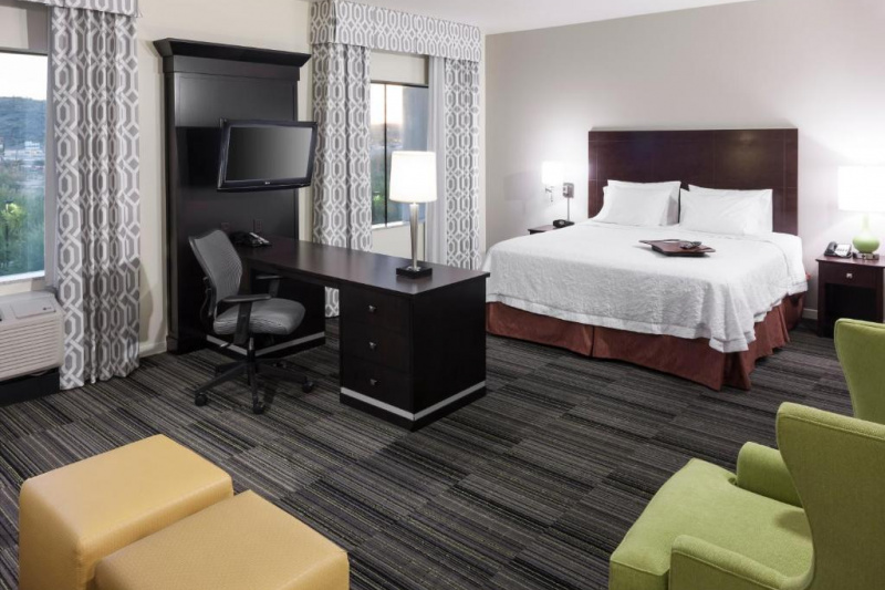 The king studio suite has a king-sized bed, wall-mounted TV, desk and seating area with an armchair and footstools.