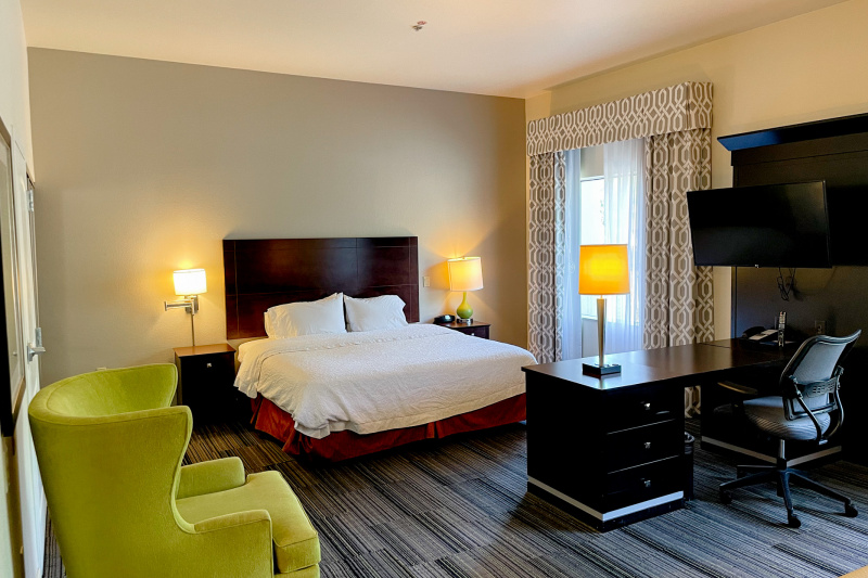 The king studio suite has a king-sized bed, wall-mounted TV, desk with executive chair and a seating area with armchair.