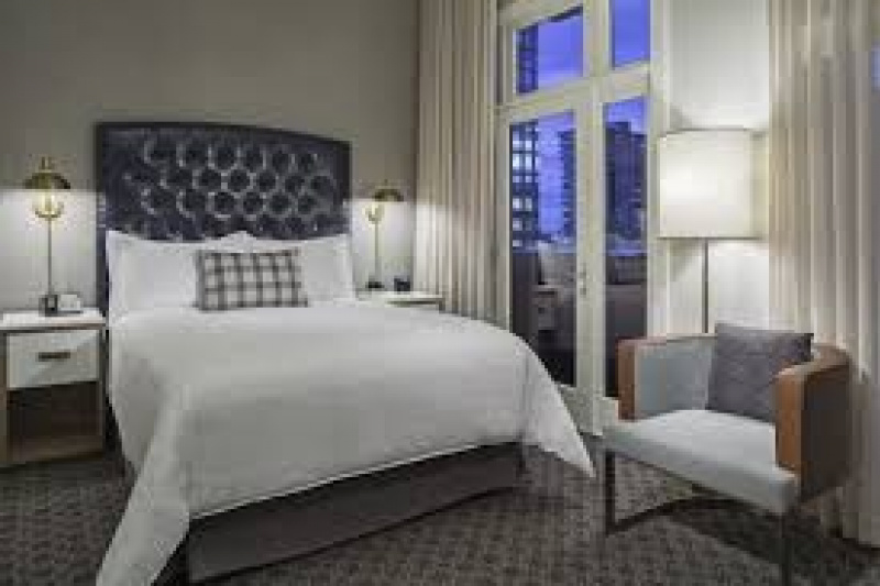Superior queen with balcony. Queen-sized bed with dark studded headboard, nightstands, French windows onto balcony, lamps, an armchair and white drapes.