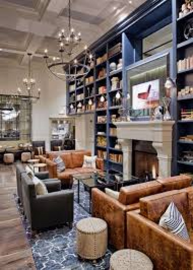 Hotel lounge has low sofa seating, coffee tables, a fireplace, bookshelves and chandeliers.