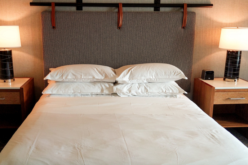 The king club guest room has a king-sized bed with white linen, fluffy pillows and a pair of nightstands with lamps and an alarm clock..