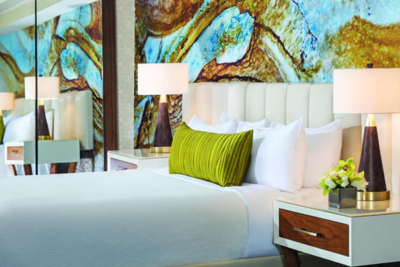 This resort king room has a king-sized bed. There are nightstands on either side of the bed with table lamps on each bed. There is a mirrored wardrobe at one side of the bed.