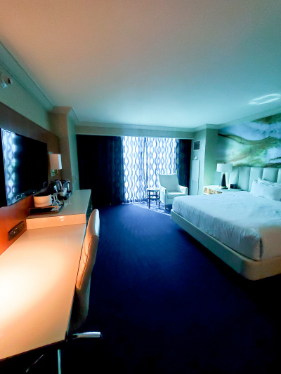 This resort king strip room has a king-sized bed. There is a full-length window. Opposite the bed is a long desk with tea and coffee-making facilities. A TV is mounted over the desk and there is a chair underneath it.