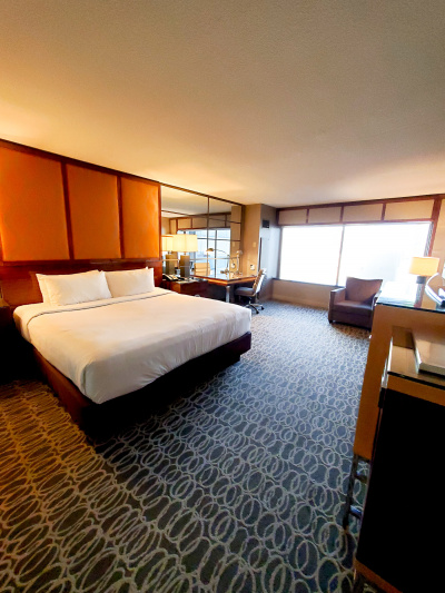 There is a king-sized bed, a console with lamp and telephone, a desk with work lamp and chair, and an armchair.