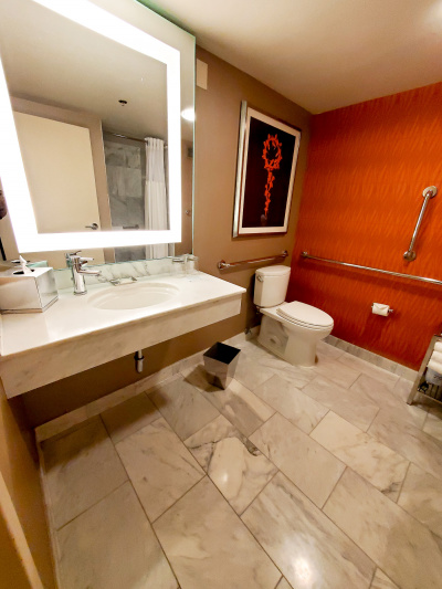 The ensuite accessible restroom has grab rails, an accessible sink with lever faucet, a large mirror and wall art.