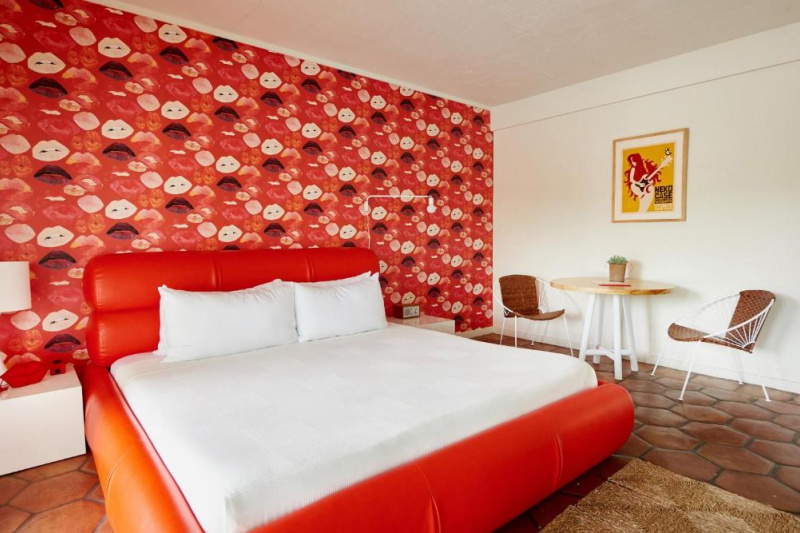 The poolside king room has a bright red king-sized bed with white linen, a table and chairs and artwork on the walls.