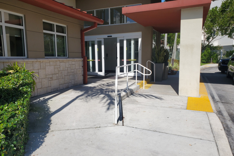 The exterior of the hotel has a covered drop-off zone and a dropped pavement and ramped access with handrails.