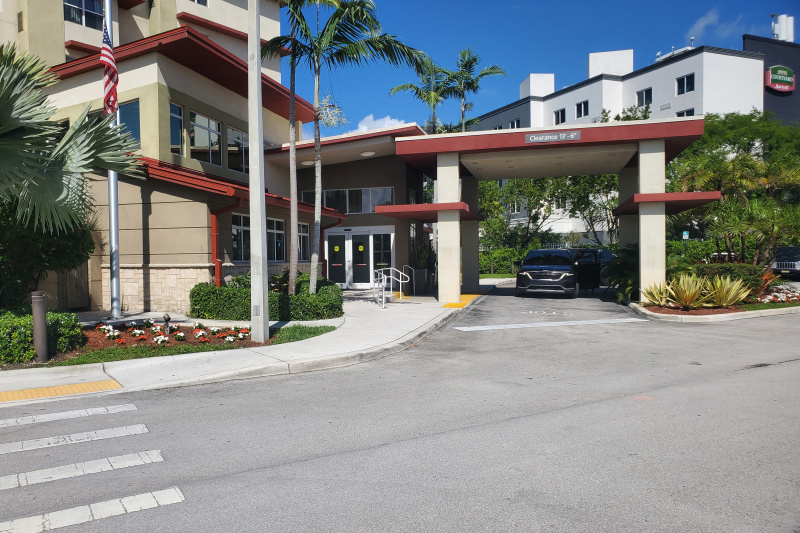 The exterior of the hotel has a covered drop-off zone and a dropped pavement and ramped access with handrails.