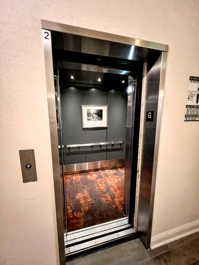 The elevator is fitted with a handrail and has artwork on the wall and a carpeted floor.