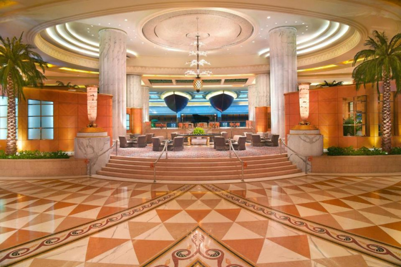 The spacious well-lit hotel lobby has 5 steps with handrails leading up to a seating area with a large round table in the middle of it.