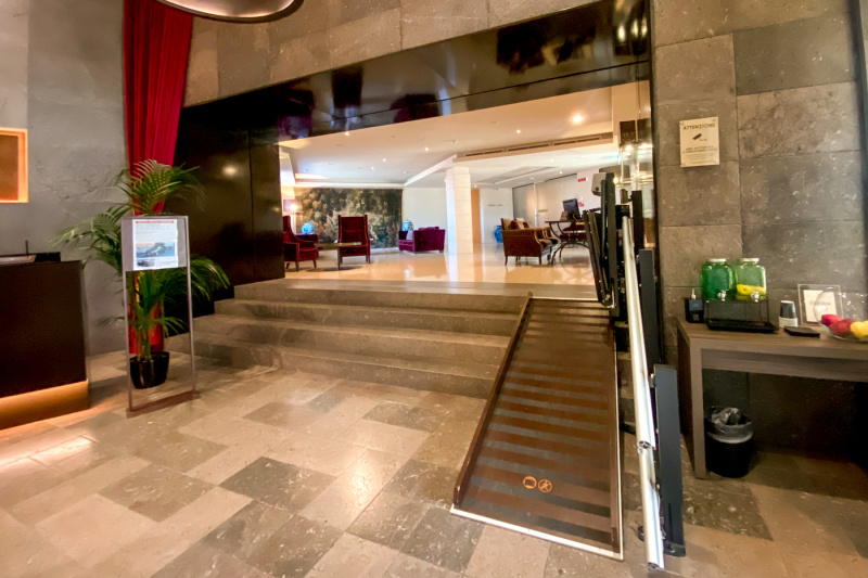 There is a ramp and chair lift for the four steps up from the reception desk to the lobby. There is a refreshment station beside the ramp. The lobby is furnished with plush armchairs, sofas and coffee tables and a smooth marble floor.