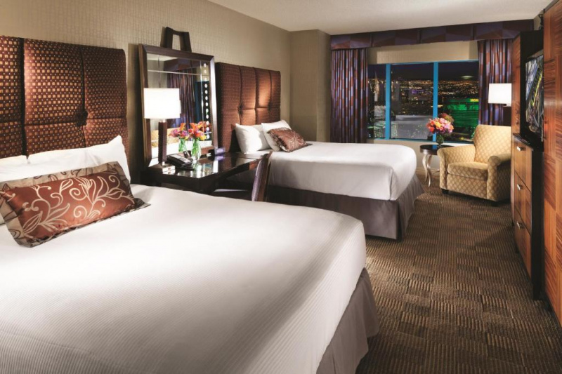 The 2 queen guest room has two queen-sized beds, a central nightstand, a lamp and a telephone. There is also an armchair with a table and a flat-screen TV.