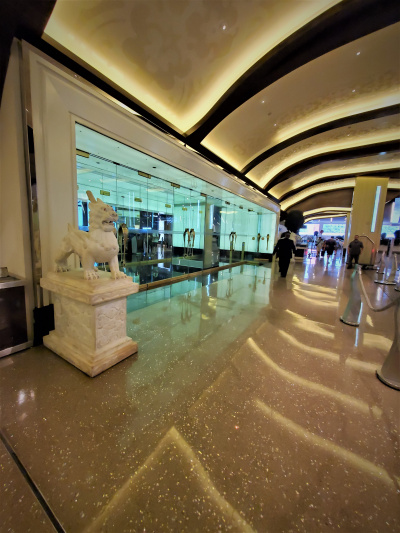 The wide corridor has a brightly lit ceiling. The walkway is step-free and there is a bank of glass double doors to one side.