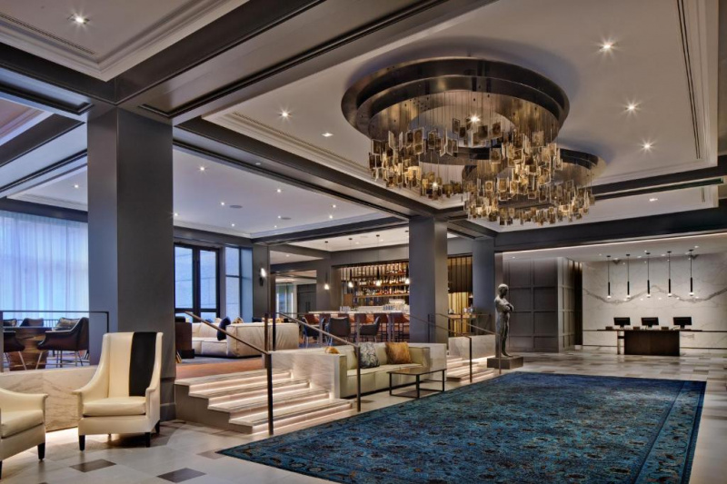 The lobby is large, with reception desks along one wall. There are 2 L-shaped sofas, several sets of tables and chairs. There are chairs going down at the far end of the room.