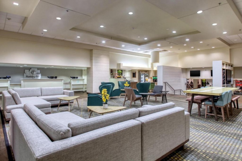 The lobby is large, with reception desks along one wall. There are 2 L-shaped sofas, several sets of tables and chairs. There are chairs going down at the far end of the room.