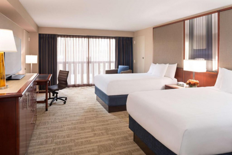 This room has 2 double beds, a nightstand with a lamp, a large work desk and chair, and a cabinet with flat-screen TV. There is plenty of space to move around the beds.