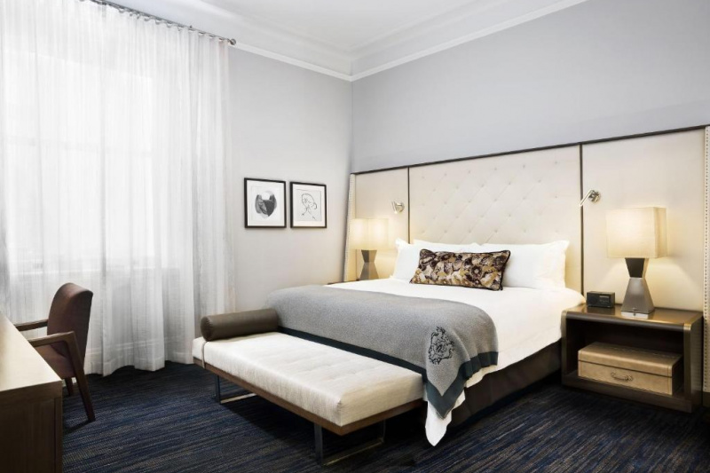 The superior suite bedroom has a king-sized bed. There are nightstands on either side of it, with table lamps on top. At the bottom of the bed is a bed bench. Opposite the bed is a desk and chair. The room is spacious and carpeted.