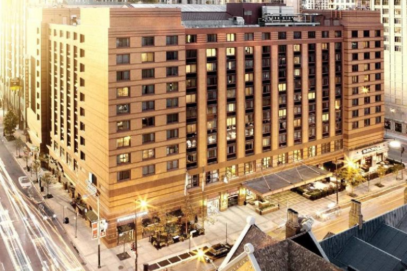 Exterior aerial view of the hotel shows the wide, spacious covered step-free entrance from the sidewalk. The hotel is huge and 9 stories high.