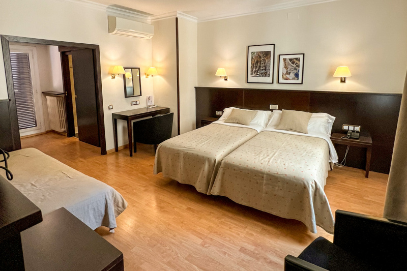 This spacious triple room has 2 single beds pushed together with nightstands on either side. One nightstand has a push-button phone on it. There is a small desk and movable chair with a third single bed opposite.