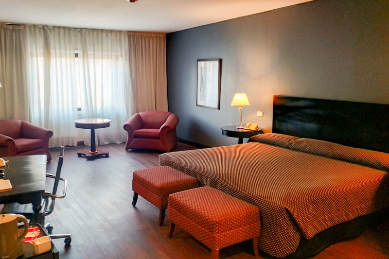 The room has a king-sized bed with nightstands, a telephone and a lamp. There are also 2 comfortable armchairs, 2 footstools, a small table, a workstation, and a movable office chair.