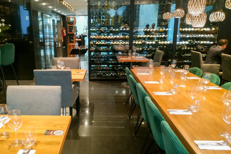 The dining area has several sets of tables and a wine store at the side of the room. There is space between the movable tables and chairs.