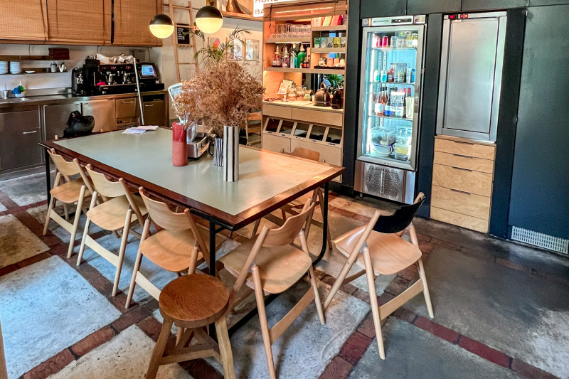 The dining area has an 8-seater table. There is a drinks fridge, coffee machine, and other kitchen units.