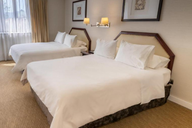 The spacious twin room has 2 queen-sized beds. There is a nightstand between the beds with wall-mounted lights above it.