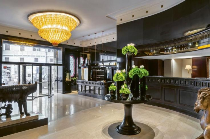The lobby is large, with a marble floor. It is accessed through either a large revolving door or large single doors to either side.  There is a reception desk to one side of the doors and another desk on a higher level.